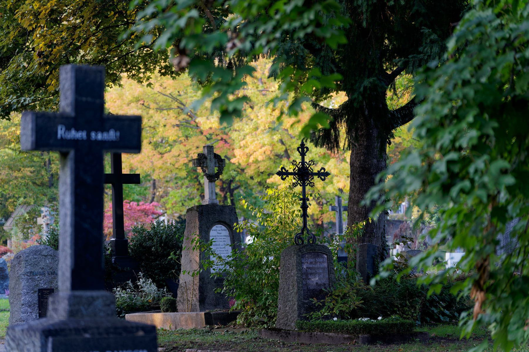 Historische Grabkreuze aus Stein und Eisen unter herbstlichem Blätterdach auf Pragfriedhof Stuttgart